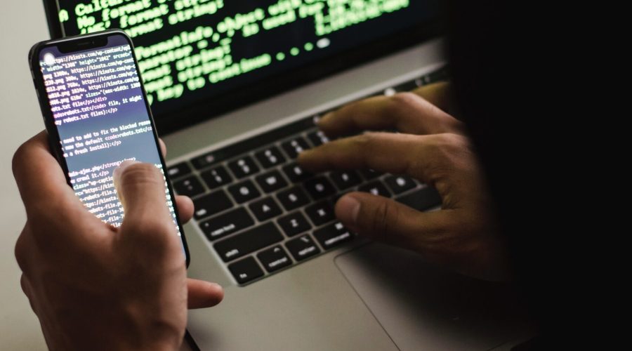 Free Unrecognizable hacker with smartphone typing on laptop at desk Stock Photo