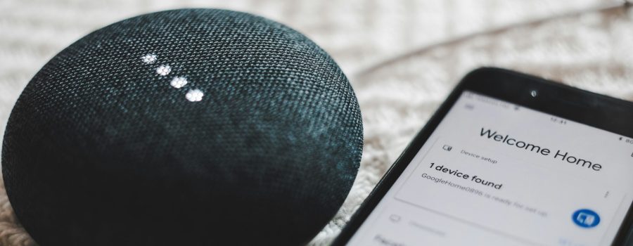 turned-on charcoal Google Home Mini and smartphone